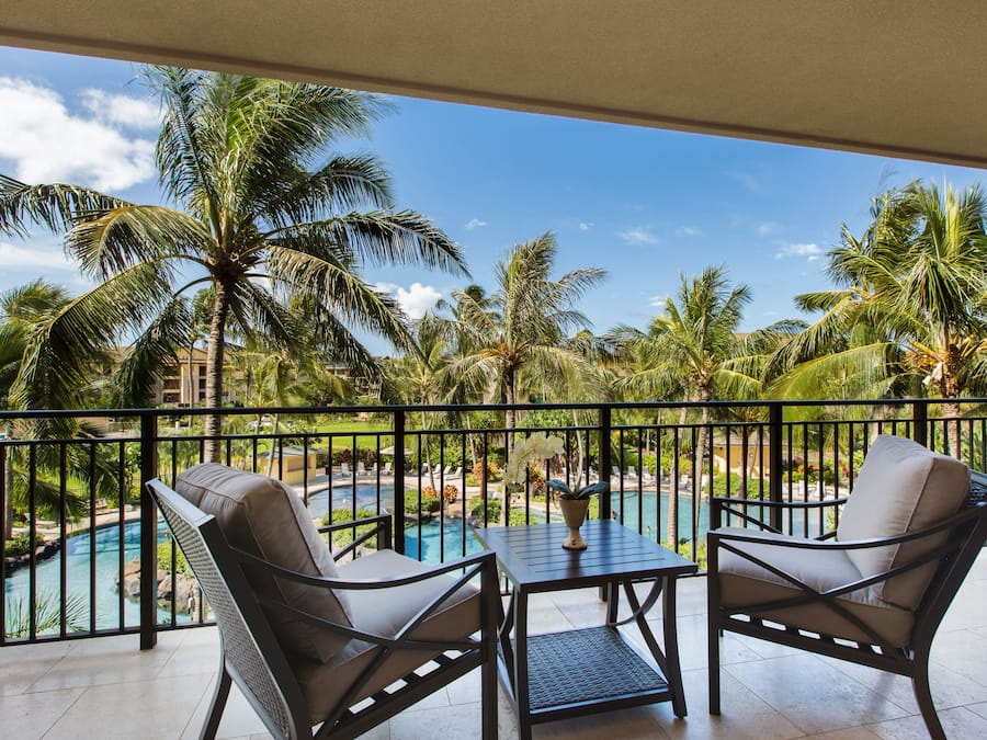 Un balcon avec deux chaises, une table et une vue sur une piscine entourée de palmiers.