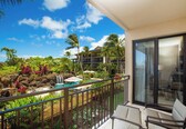 A balcony with a view of a tropical resort, including a pool, palm trees, and a waterfall.