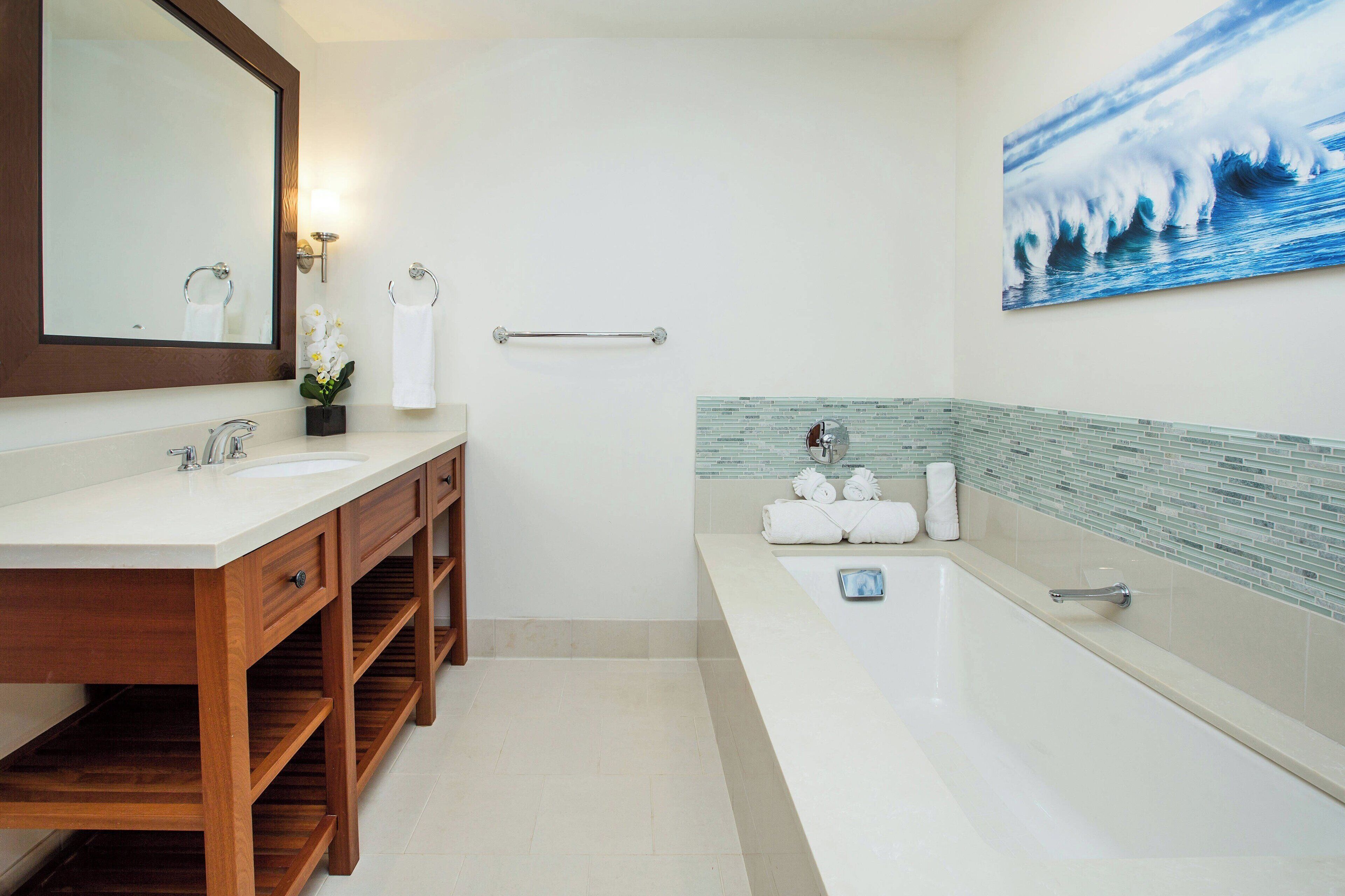 Un baño moderno con tocador de madera, un espejo grande, una bañera y una zona de ducha con azulejos.