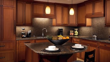 A kitchen with wooden cabinets, granite countertops, a central island with seating, and pendant lighting.