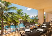 A dining area with a table set for two, overlooking a pool and palm trees.
