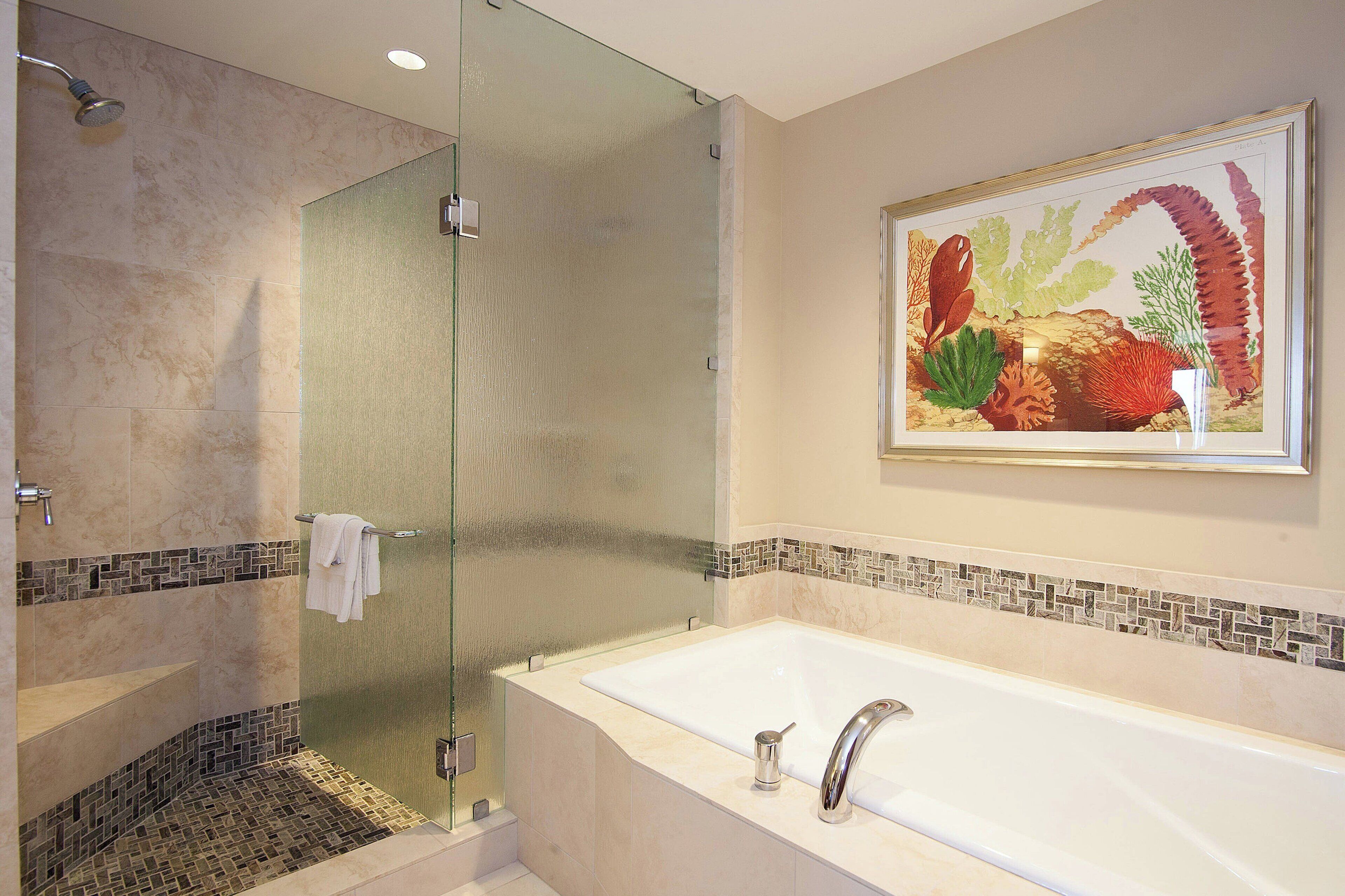 A bathroom with a glass shower enclosure, a white bathtub, and a mosaic tile border.
