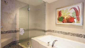 A bathroom with a glass shower enclosure, a white bathtub, and a mosaic tile border.
