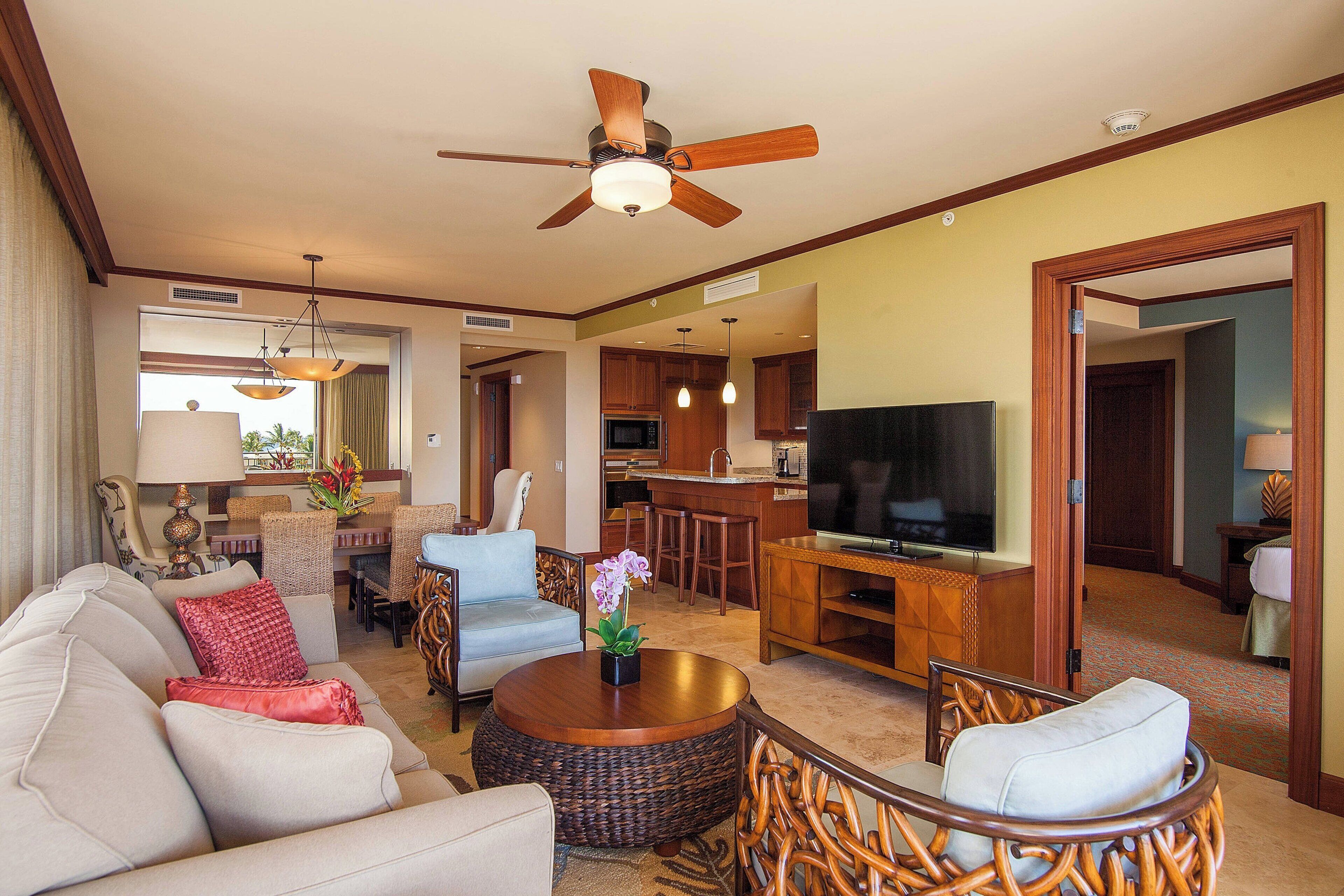 A spacious living area with a ceiling fan, a television, and a dining area with wicker furniture.