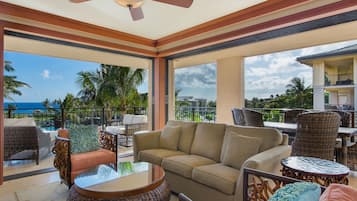 A spacious balcony with a view of the ocean, furnished with wicker chairs, a sofa, and a round table.
