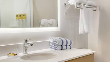 A modern bathroom with a white sink, chrome faucet, and a mirror above it. There are white towels on a rack and a folded towel on the counter.