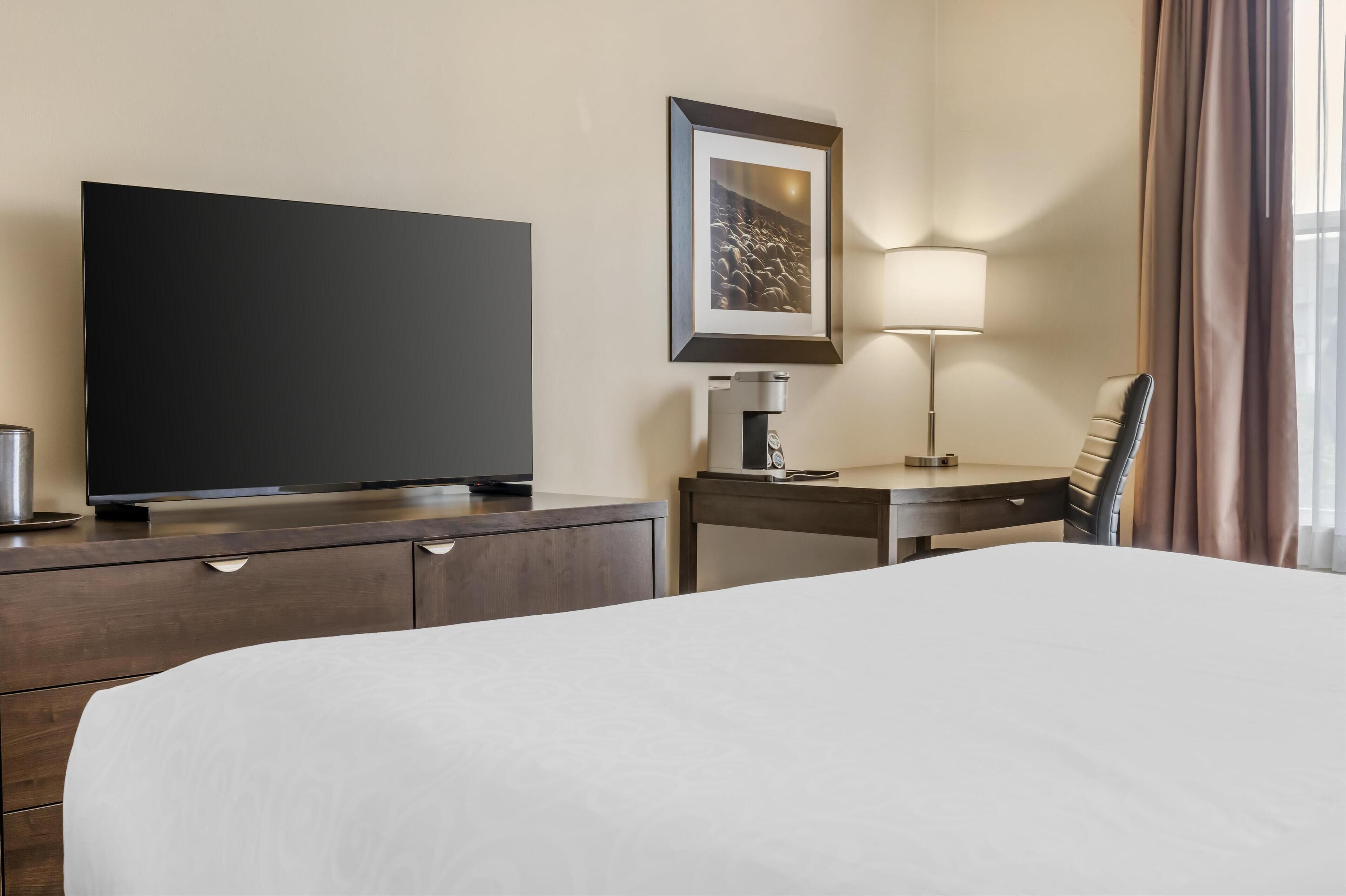 Habitación de hotel con una cama grande, un televisor de pantalla plana, un escritorio con lámpara y un cuadro en la pared.