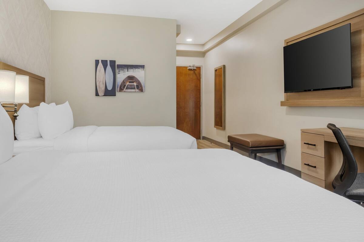 A hotel room with two beds, a desk, a chair, a television, and a small stool.