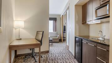 Una habitación de hotel pequeña con kitchenette, una pequeña mesa de comedor con una silla, un sofá y una lámpara.