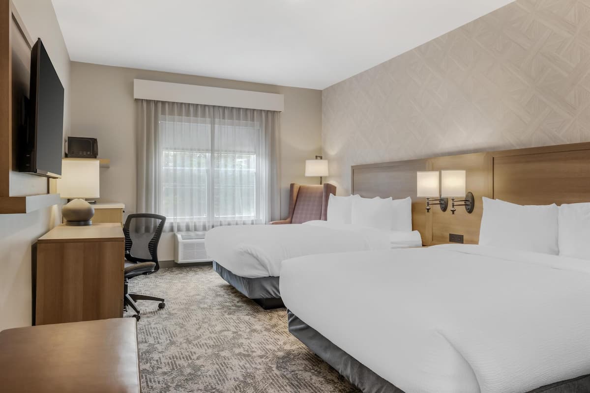 A hotel room with two beds, a desk, a chair, a TV, and a window with curtains.