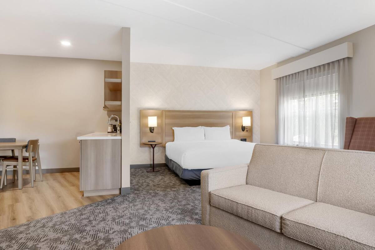 A hotel room with a bed, a sofa, a desk, and a small kitchenette.