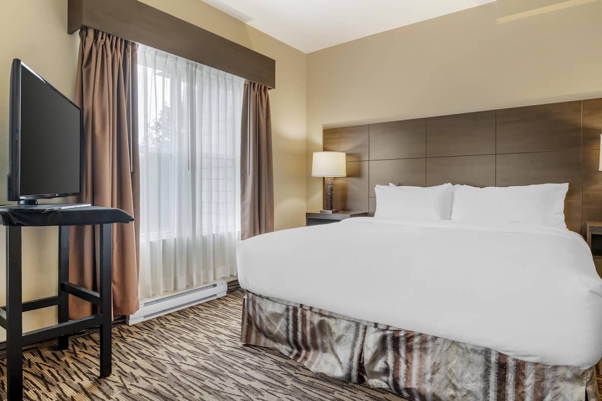 A hotel room with a large bed, a flat-screen TV, a desk, and a window with curtains.