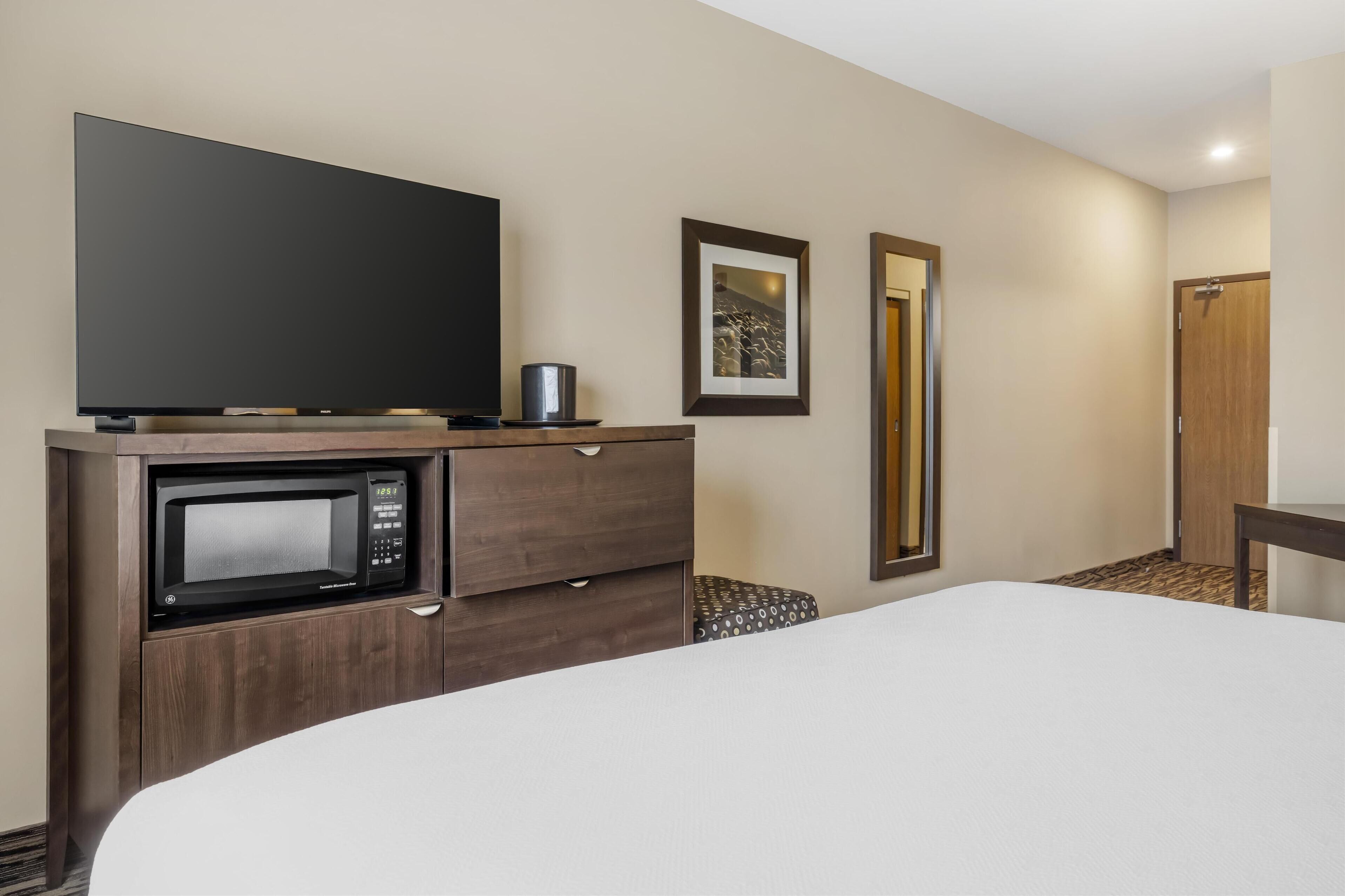 A hotel room with a bed, a TV, a microwave, a small table, and a door.