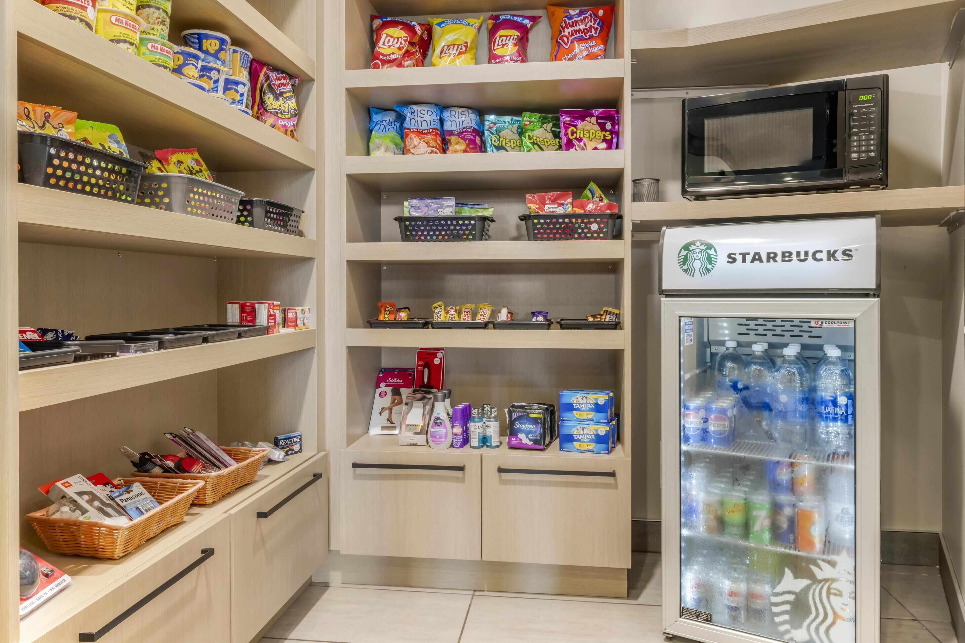 A storage area with shelves stocked with snacks, a microwave, and a Starbucks refrigerator.
