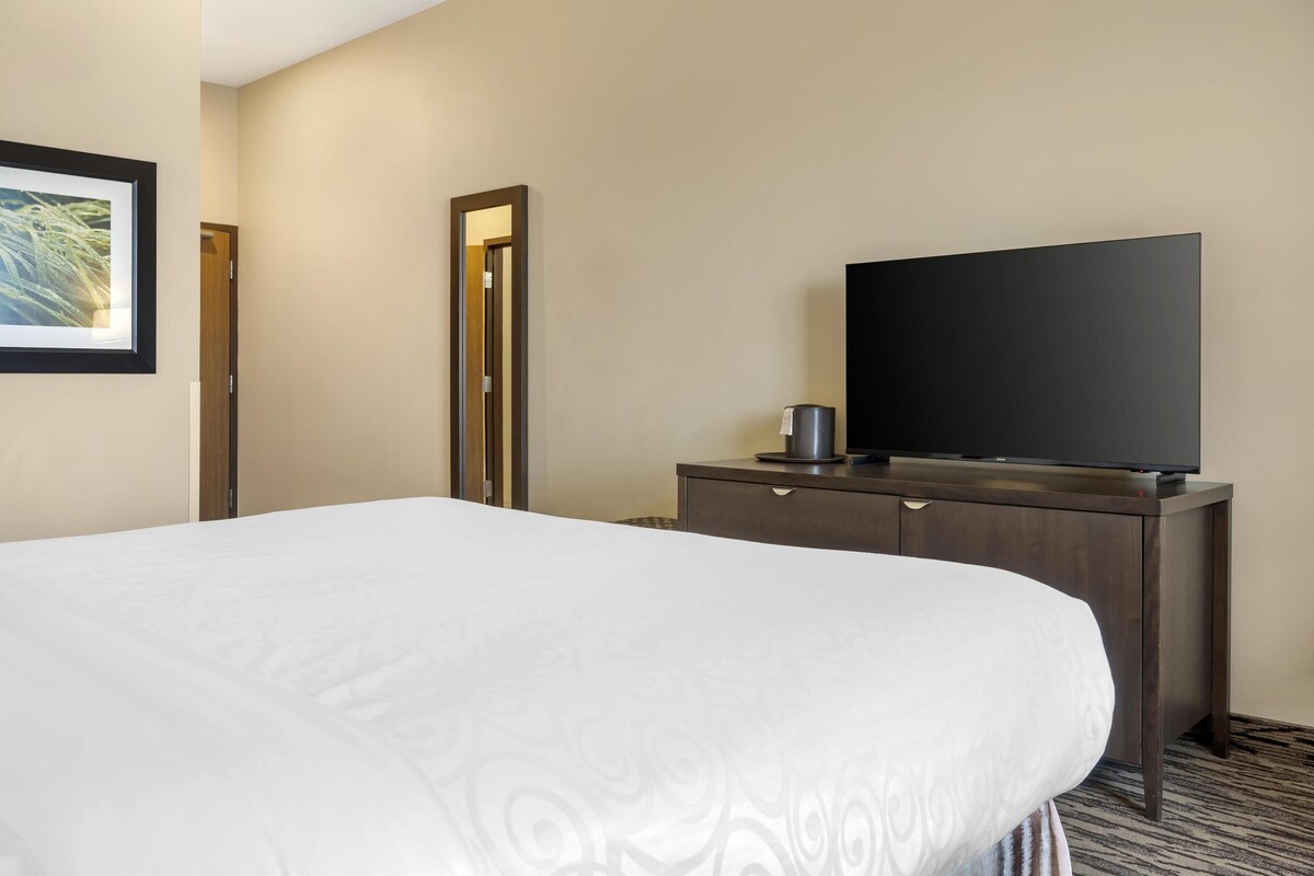 Habitación de hotel con una cama grande, un aparador de madera oscura, un televisor de pantalla plana y un espejo.