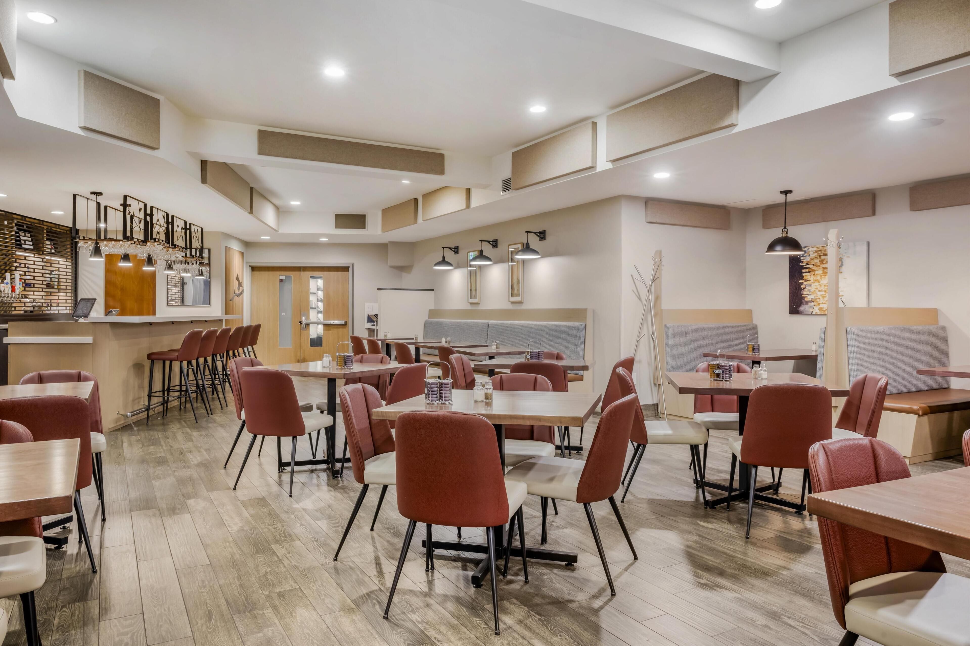 Un espace repas moderne comprenant plusieurs tables et chaises, un bar et un coin salon avec des bancs rembourrés.