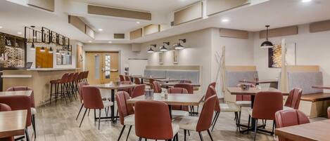 Un espace repas moderne comprenant plusieurs tables et chaises, un bar et un coin salon avec des bancs rembourrés.