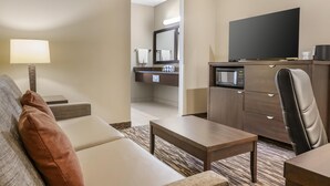 Habitación de hotel con sofá, una mesita, televisor, microondas y baño a la vista a través de una puerta abierta.