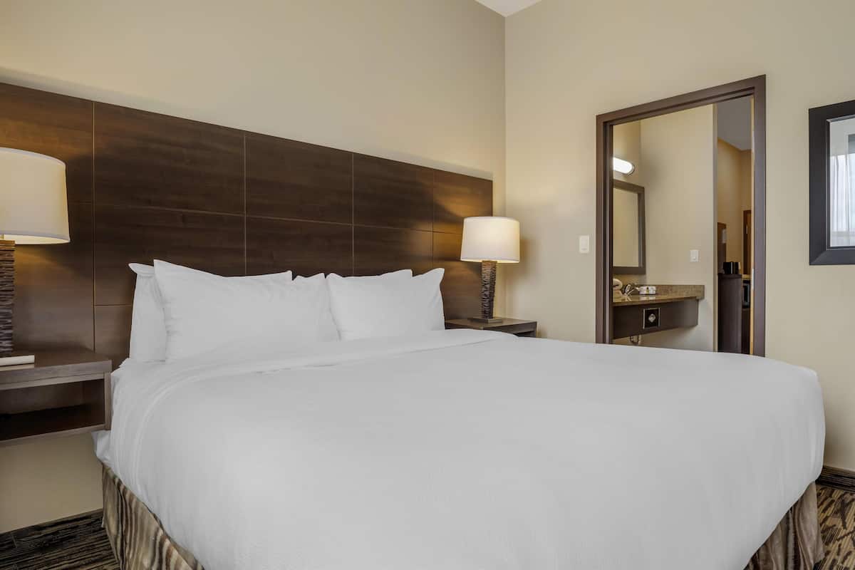 A hotel room with a large bed, two bedside tables, a nightstand, a mirror, and a wall-mounted lamp.