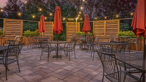 Un patio al aire libre con mesas y sillas, luces colgantes y cercas de madera.