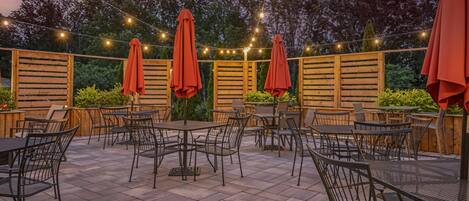Un espace extérieur aménagé en terrasse, avec des tables et des chaises, des guirlandes lumineuses et des clôtures en bois.
