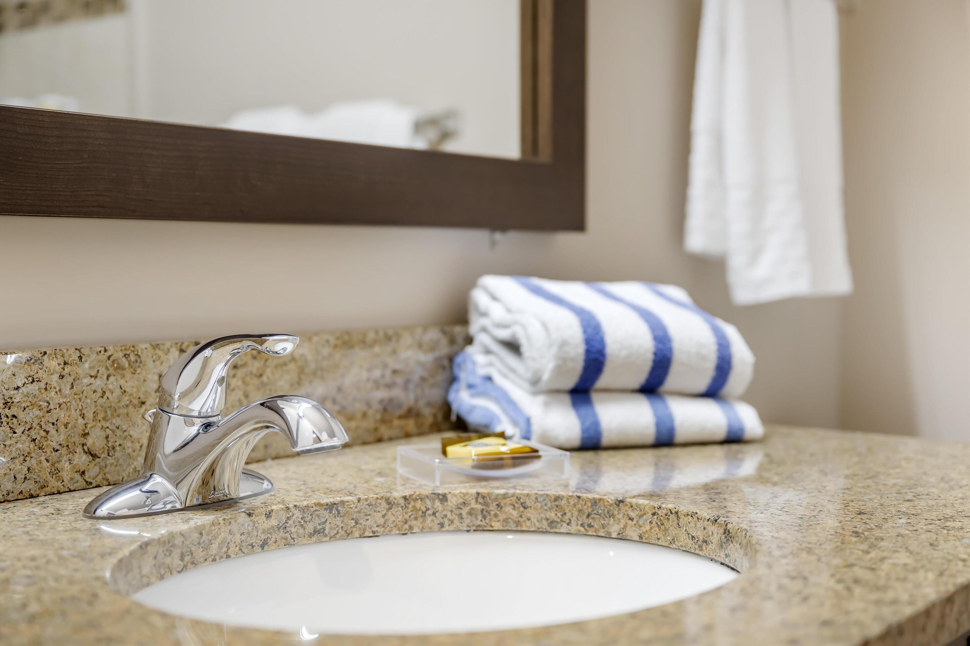A bathroom with a granite countertop, a silver faucet, a white sink, and a towel rack with folded towels.