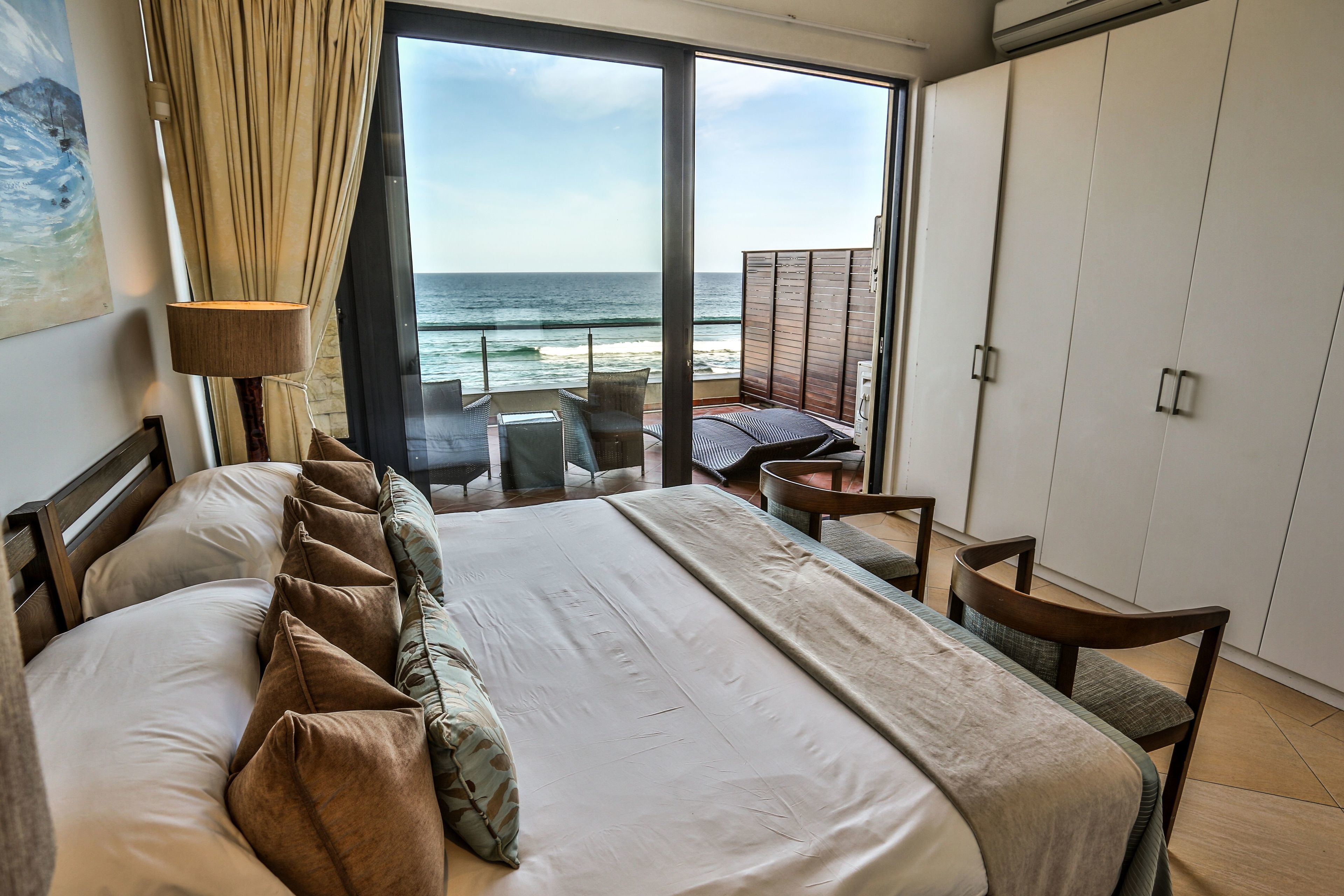 A bedroom with a large bed, a view of the ocean, and a balcony with seating.