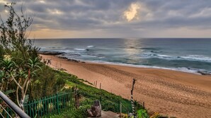 A beach with waves, a fence, and greenery. - Canelands Beach Club (Ballito)