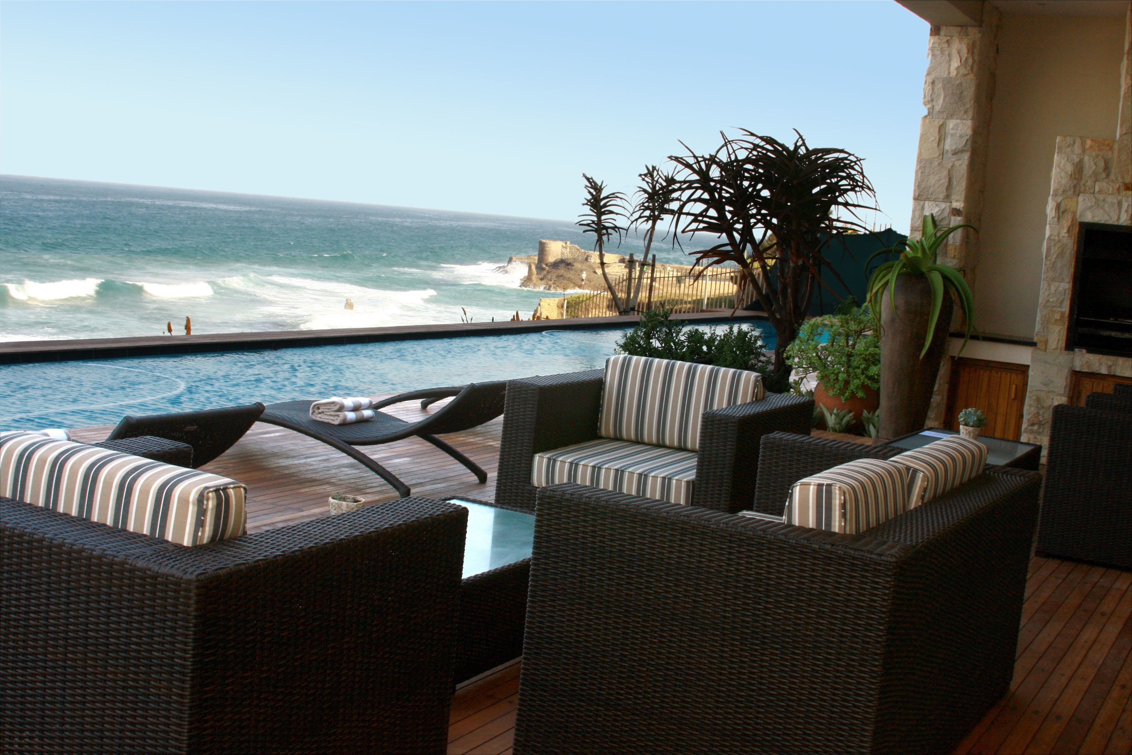 A balcony with wicker furniture, a stone wall, and a view of the ocean.