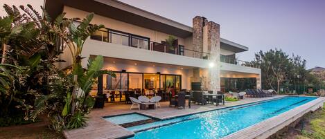 A modern hotel with a large swimming pool, outdoor seating, and a well-maintained garden.