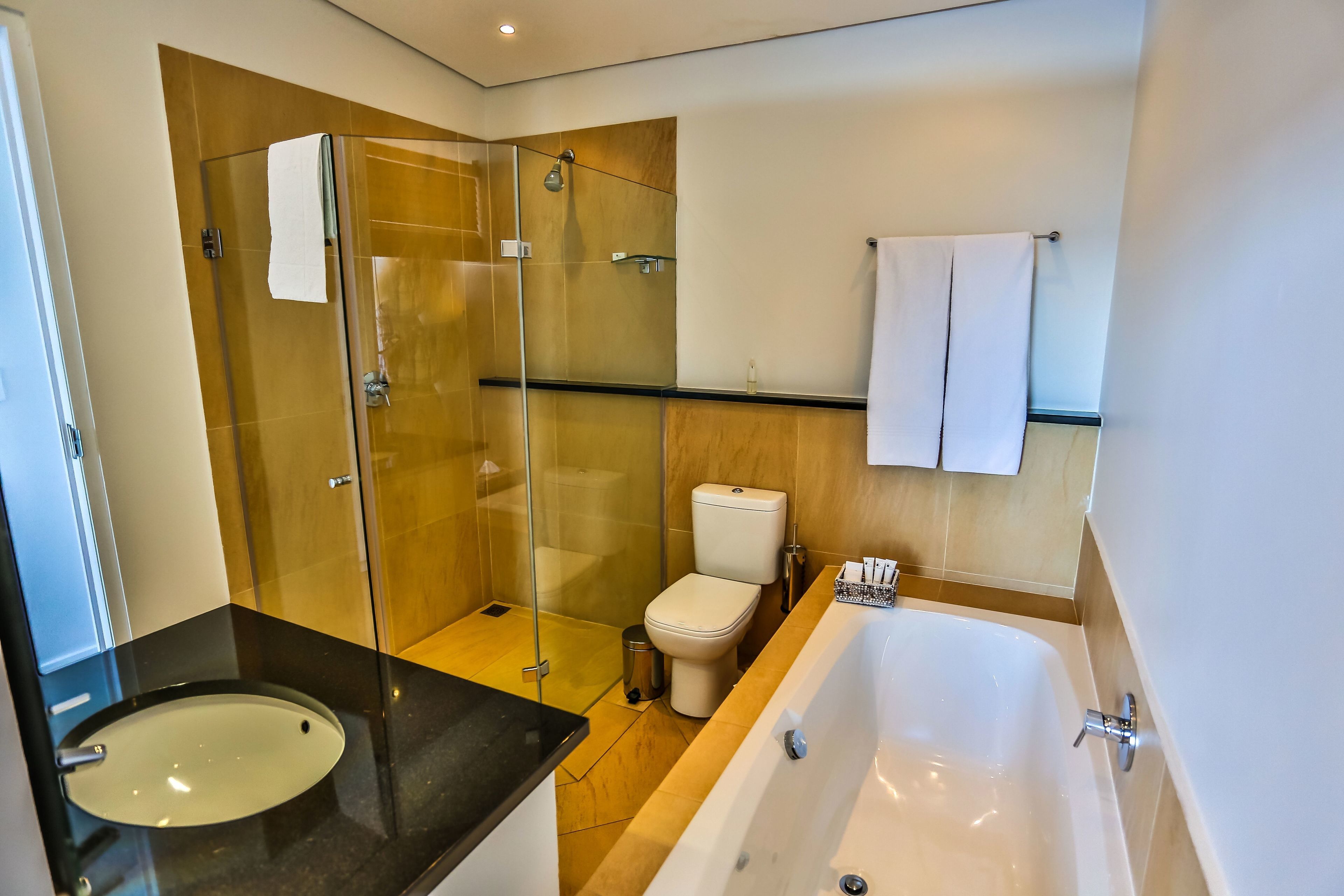 A modern bathroom with a glass-enclosed shower, a white toilet, a bathtub, and a black countertop with a sink.