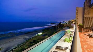A swimming pool with a view of the beach and ocean at dusk.