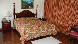 Quarto com cama de madeira, duas mesas de cabeceira com luminárias, um quadro na parede e cortina listrada.