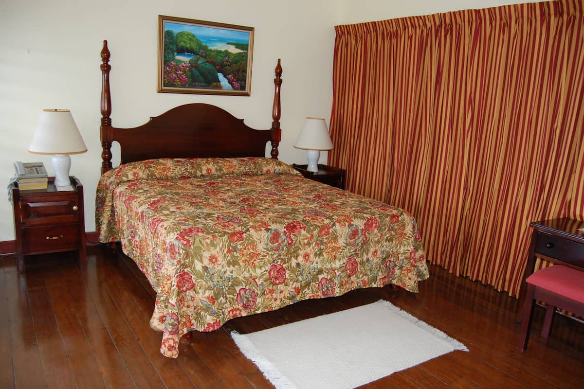 A bedroom with a wooden bed, two bedside tables with lamps, a painting on the wall, and a striped curtain.