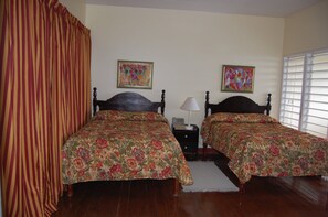 Una habitació amb dos llits, una tauleta de nit, una làmpada i dos quadres florals a la paret.
