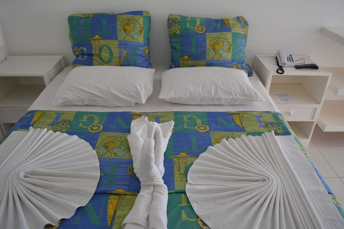 A hotel room with a bed, two pillows, a bedside table with a phone, and a neatly folded towel.