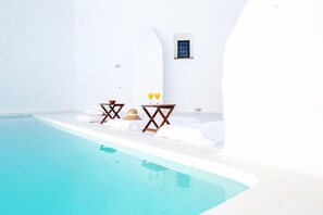 Habitación de paredes blancas con piscina, una mesa pequeña con un vaso y una ventana.