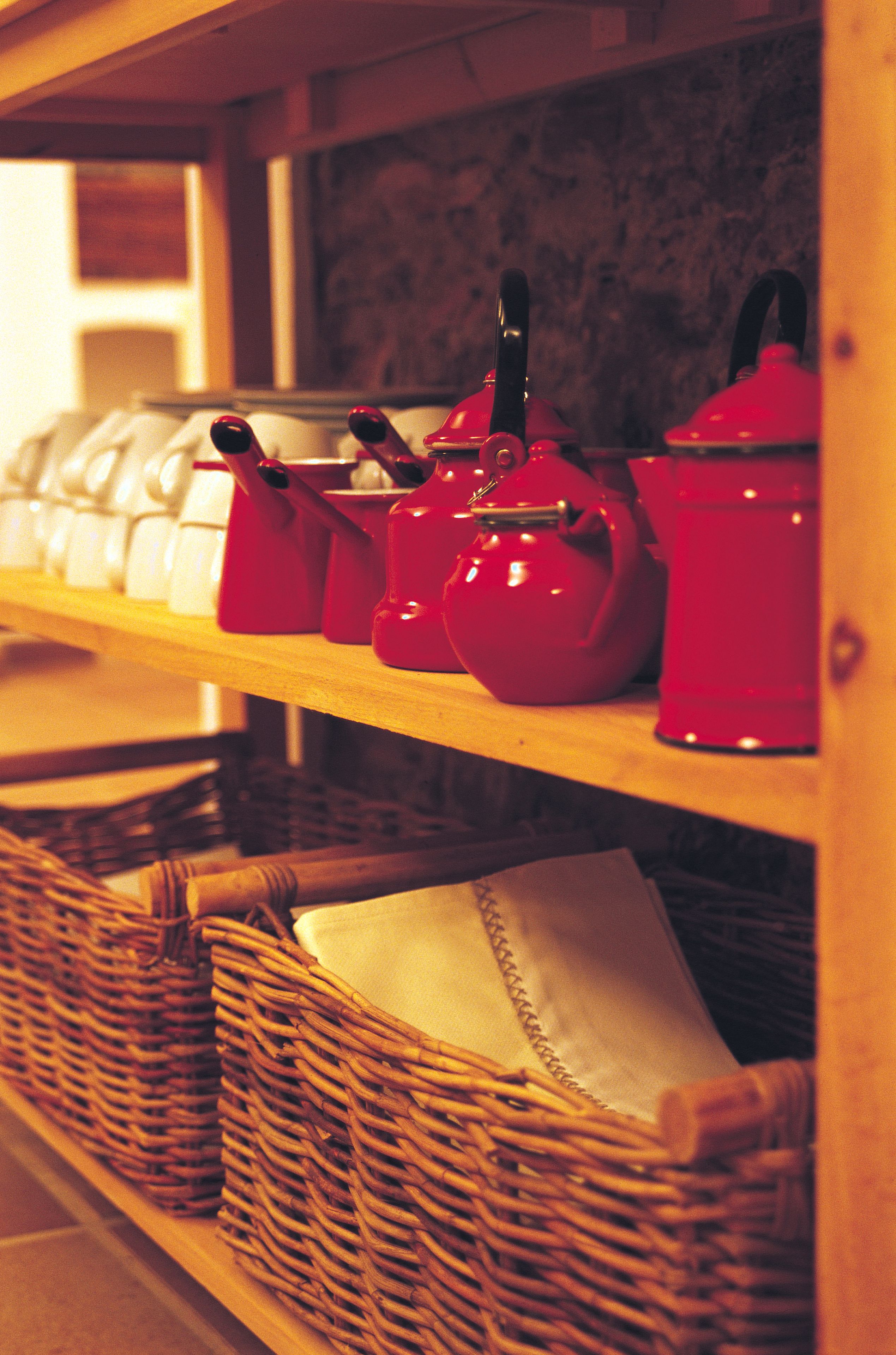 Una repisa de cocina con teteras rojas y cestas de mimbre.