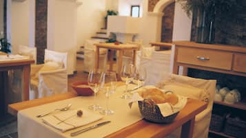 Un comedor con una mesa dispuesta para dos personas, que incluye un cesto de pan, copas de vino y cubiertos.