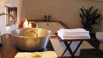 Une salle de bain avec un grand lavabo en métal, une pile de serviettes blanches, une bougie allumée et une plante en pot.