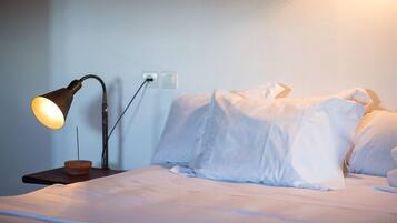 A neatly made bed with white linens, a bedside lamp, and a small wooden nightstand.