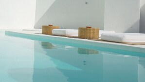Una piscina con agua azul cristalina, dos cestas de mimbre y una pared blanca.