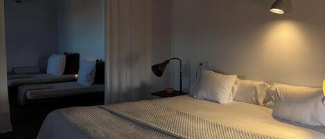 Un dormitorio con una cama grande, una mesita de noche con lámpara y una pequeña mesa con un bol.