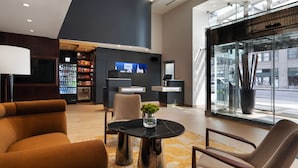 A modern lobby with a reception desk, seating area, and a large window offering a view of the street. - Courtyard by Marriott New York Manhattan/SoHo (New York)