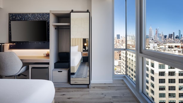 A modern hotel room with a large bed, a desk, a chair, a TV, and a city view. - Courtyard by Marriott New York Manhattan/SoHo (New York)