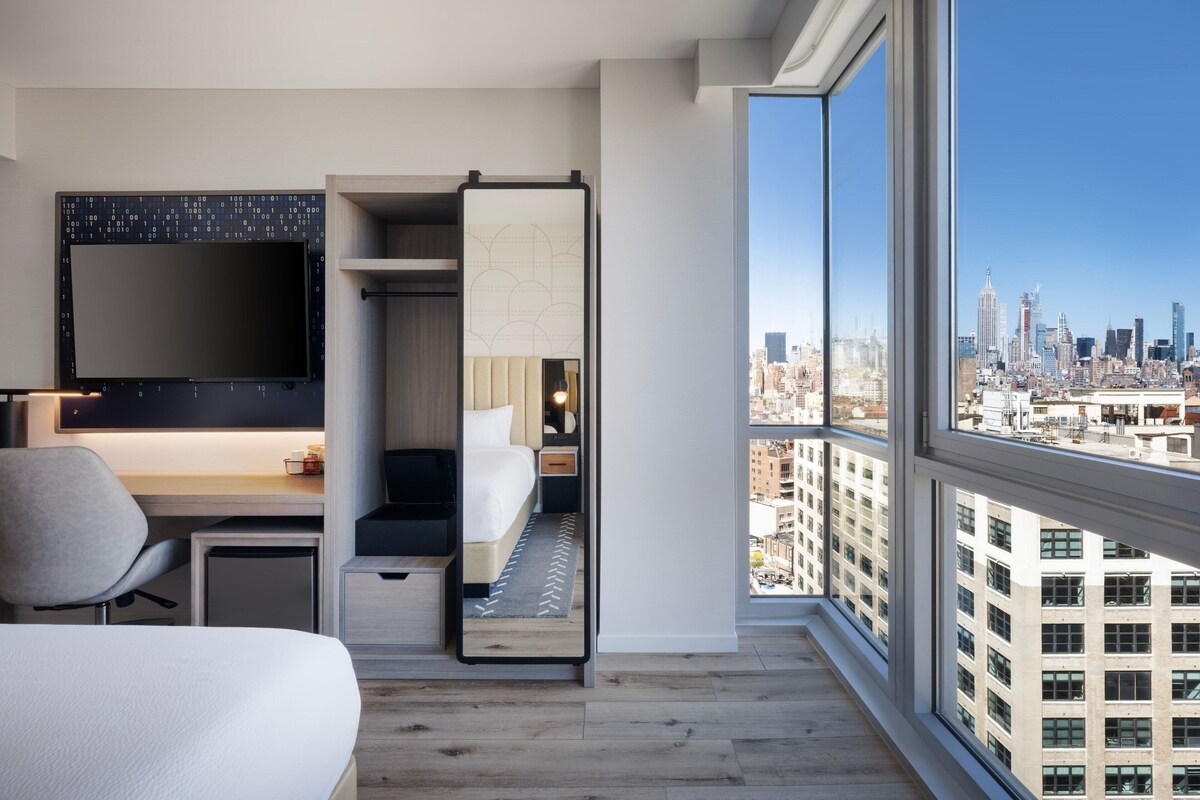 Une chambre d’hôtel moderne dotée d’un grand lit, d’un bureau, d’une chaise, d’une télévision et offrant une vue sur la ville.