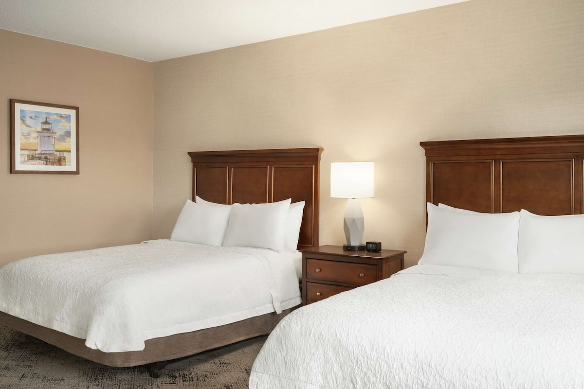 A hotel room with two beds, a nightstand with a lamp, and a framed picture on the wall.