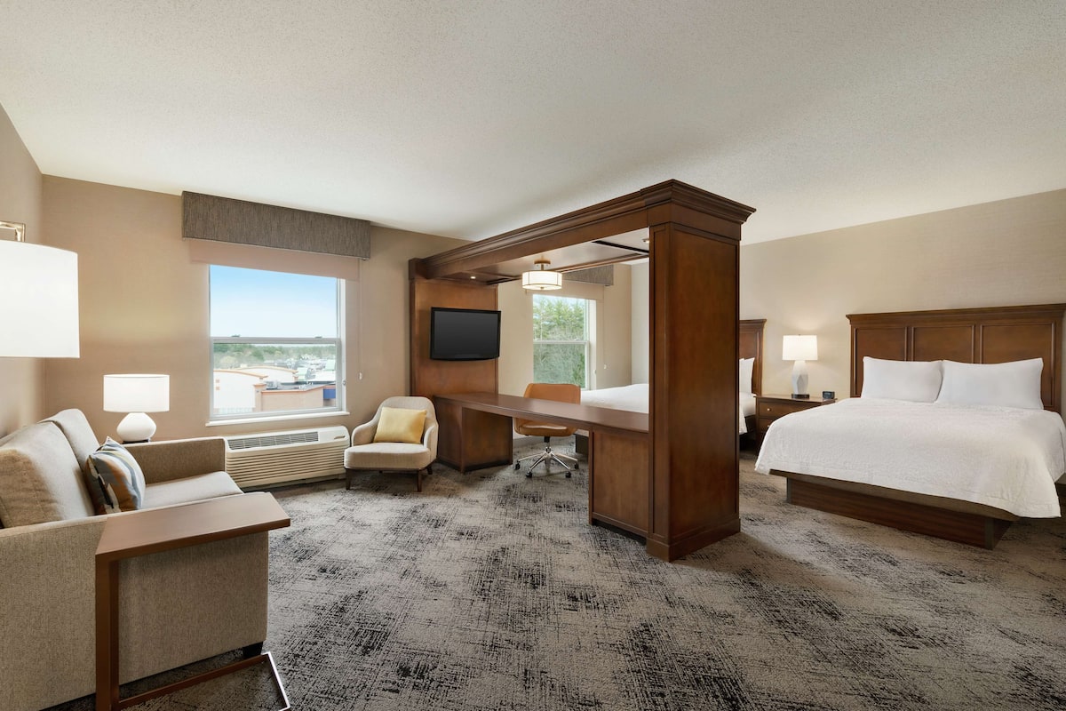A hotel room with a large bed, a desk, a chair, a sofa, and a TV.