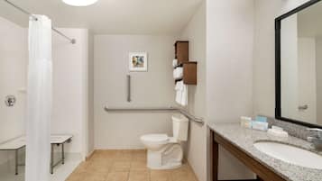 Une salle de bain moderne avec des toilettes blanches, une douche avec un rideau blanc, une barre d’appui, un lavabo avec un miroir et un porte-serviettes.