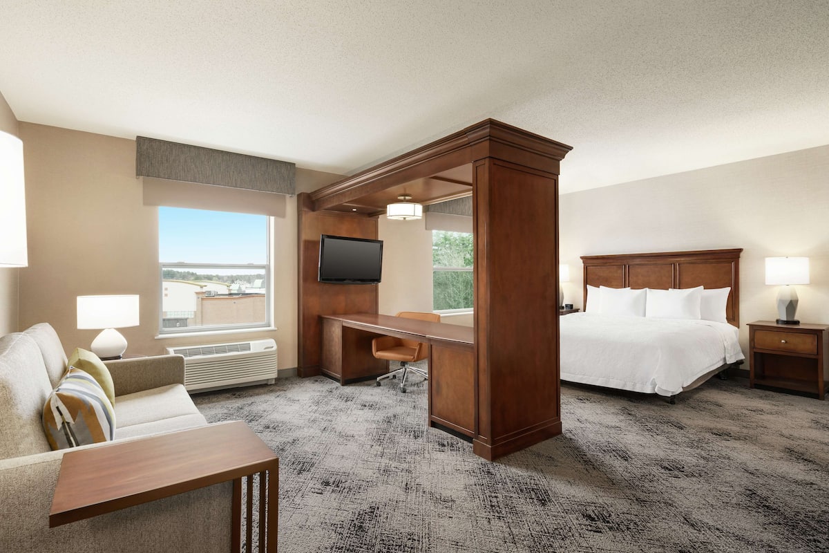 A hotel room with a bed, desk, and chair, a TV, and a view of the city.